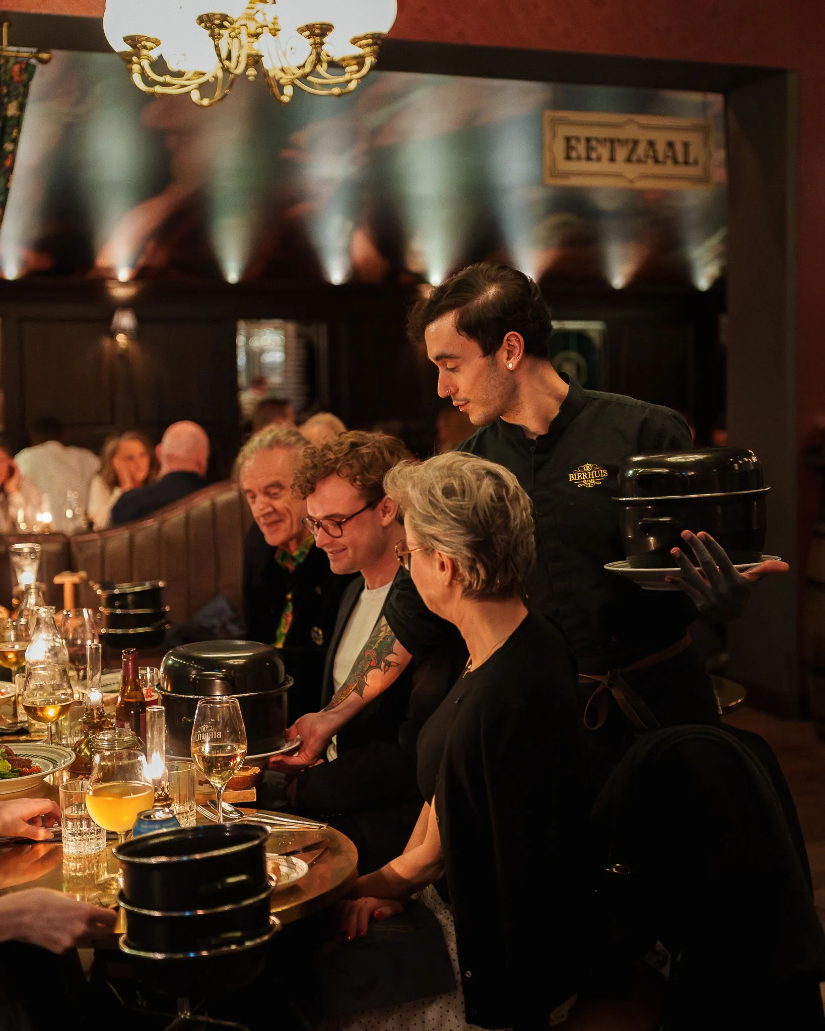 Servitör serverar ölgrytor vid ett långbord i matsalen Eetzaal på Bierhuis i Uppsala