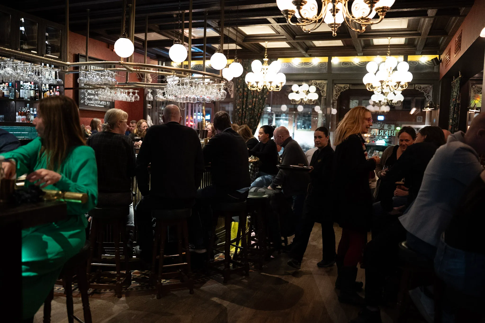 Fullsatt bar på Bierhuis en kväll, gäster längs disken under ljuskronorna